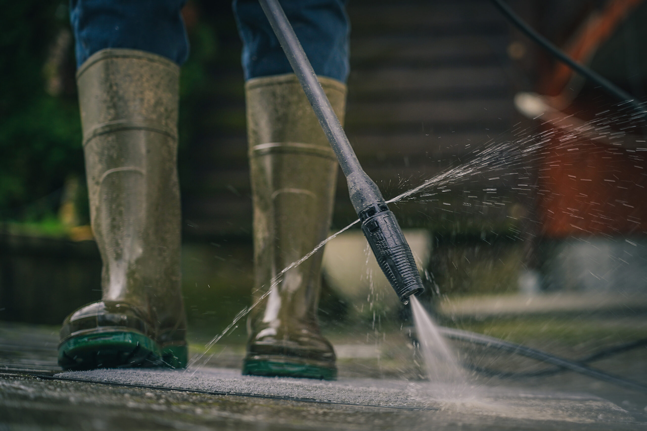 Person cleaning a rug or floor mat with the use of a high pressure water cleaner. Cleaning mats with high pressure jet while wearing plastic boots