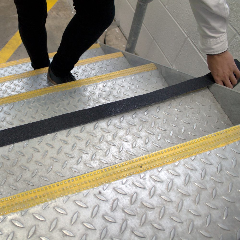 Image-of-a-person-applying-black- Gripfoot-conformable-to-a-stair-edge