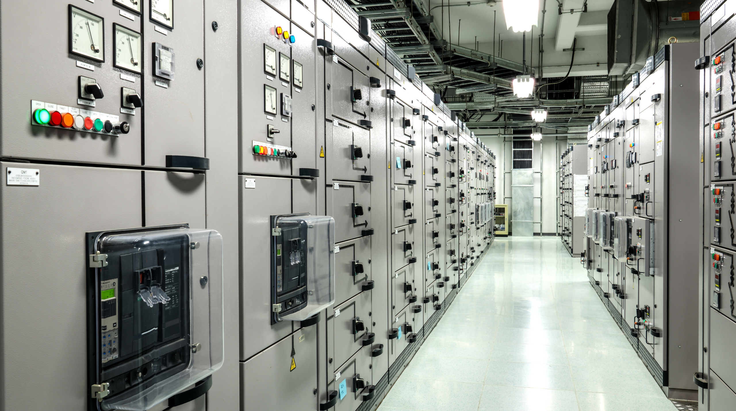 Electrical switchroom with rows of industrial control panels and switchgear.